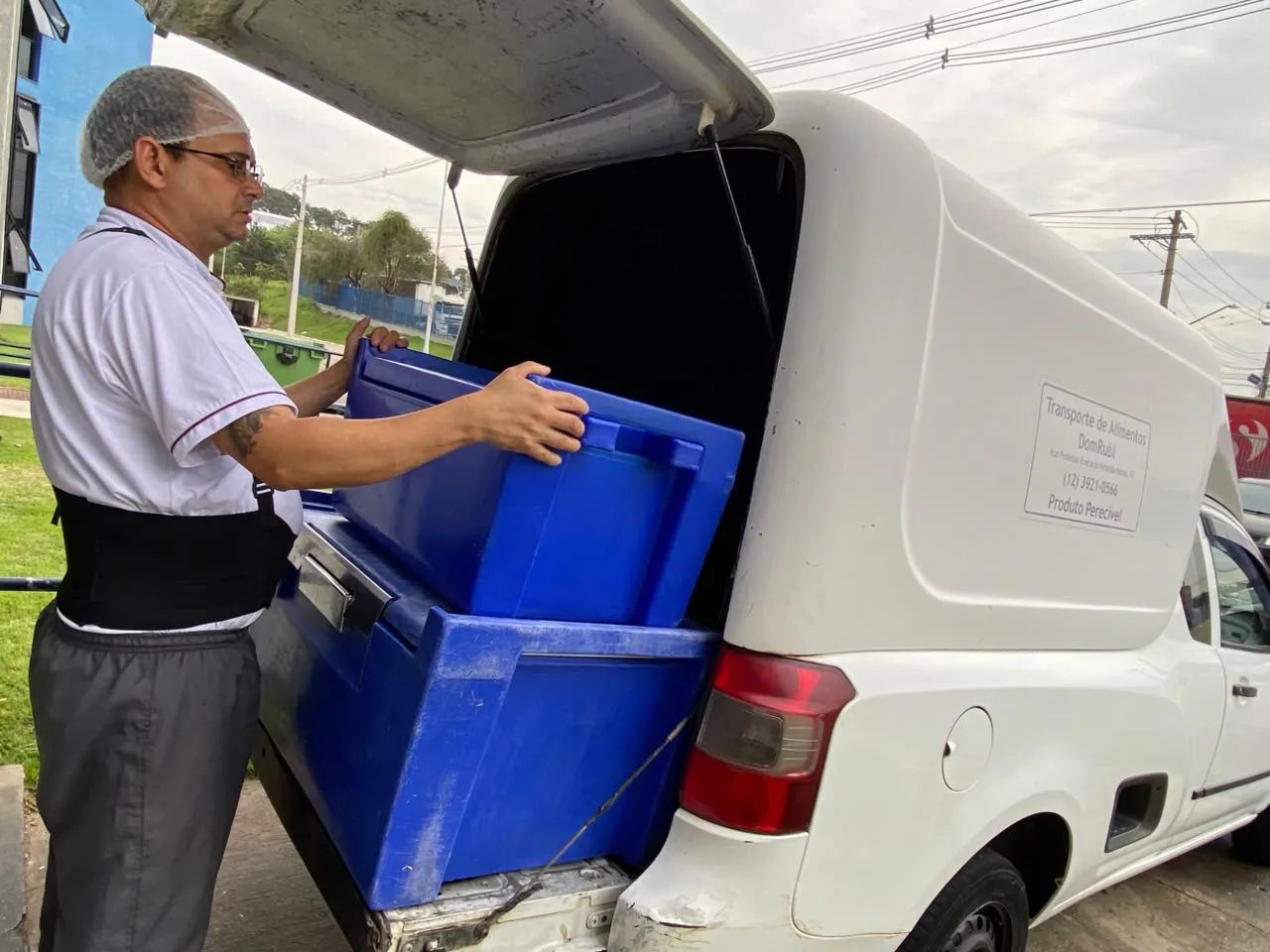 Entregador da Dom Rubi carregando caixa térmica hotbox azul em veículo de entrega