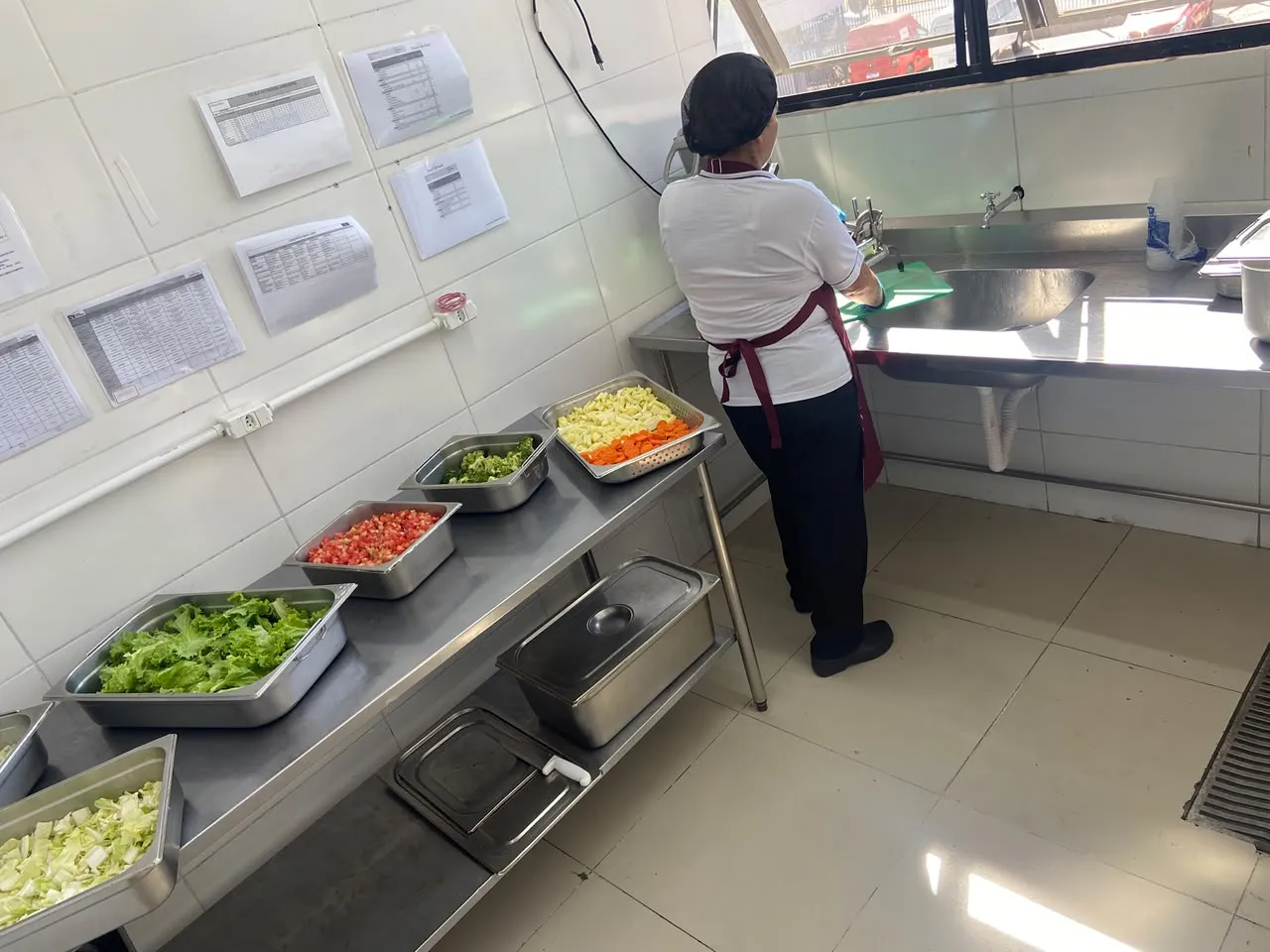 Profissional da Dom Rubi com touca e avental preparando saladas frescas em bancada de inox